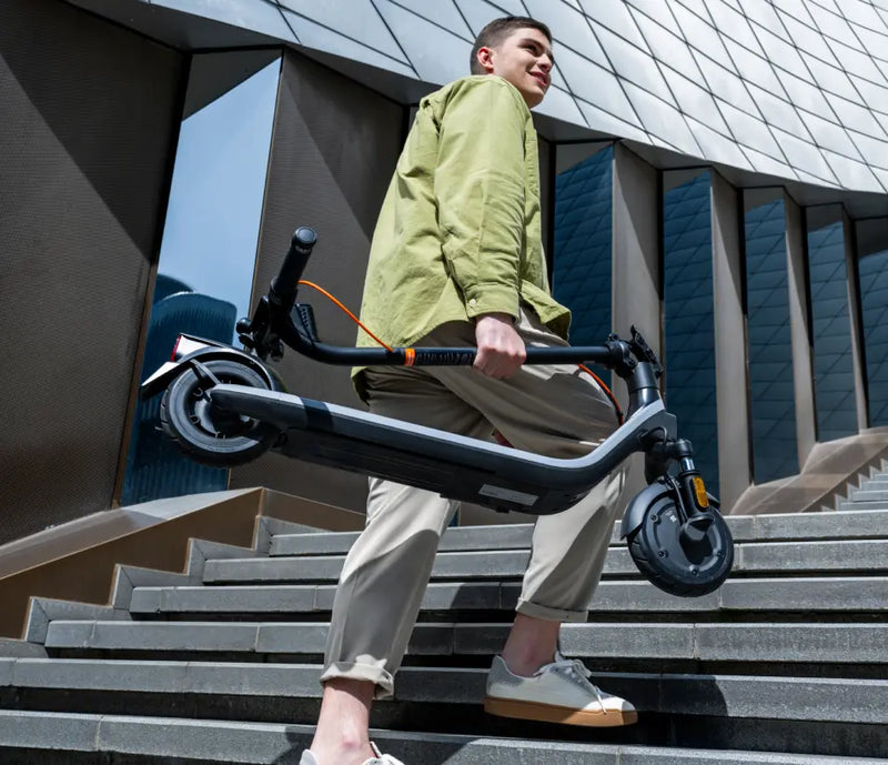 Homme portant la trottinette pliée Segway Ninebot E2 Plus E II dans un escalier