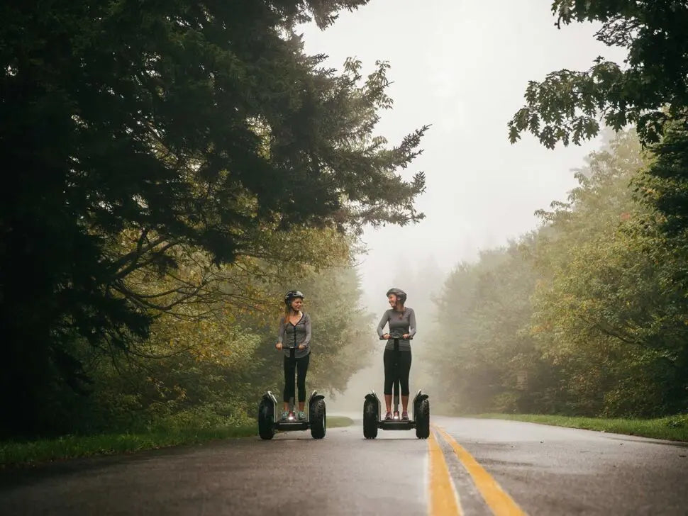 Deux personnes sur des gyropodes Segway X2 SE sur une route forestière brumeuse